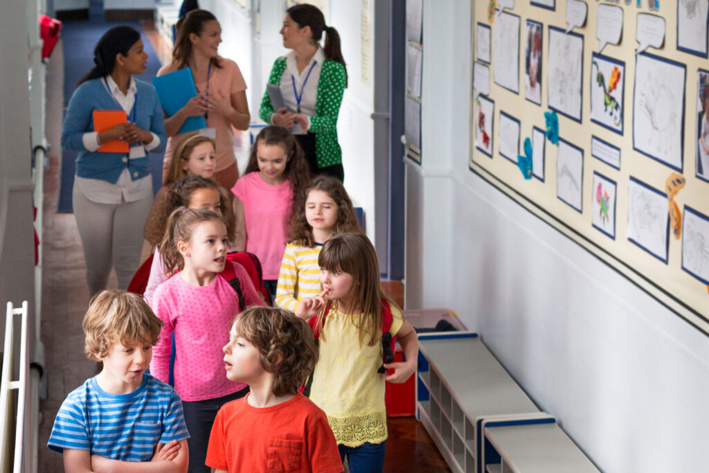 Three teachers and a group of children walking down a corridor in school.